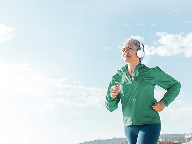 Woman wearing white headphones running outdoors on a sunny day