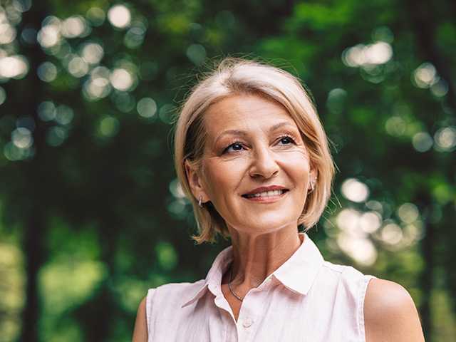 Smiling white woman stands in front of trees, looking into the distance