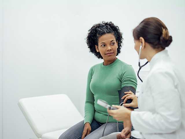Black woman in a green shirt sits in an exam room and speaks with a Corewell Health interventional radiology specialist