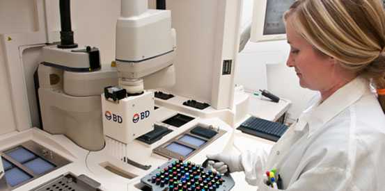 A woman wearing a lab coat presents a tray, indicating a hands-on approach to her research or project.