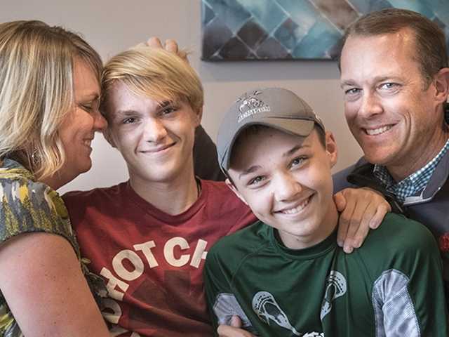 Smiling mother and father hug their two teenage sons