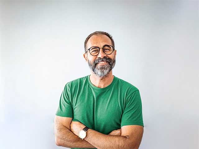 Smiling white man with a grey beard and glasses crosses his arms