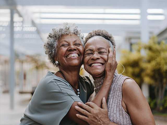 Two smiling older Black women hug each other while standing together