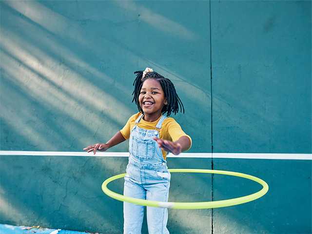 Young girl hula hopping outside at a park.