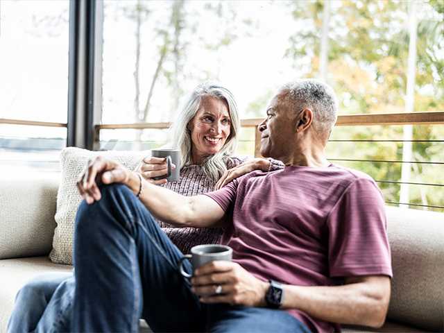man and woman sitting in chairs outside on a porch drinking coffee