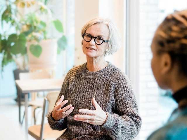 Older white woman with short grey hair speaks among a group of people
