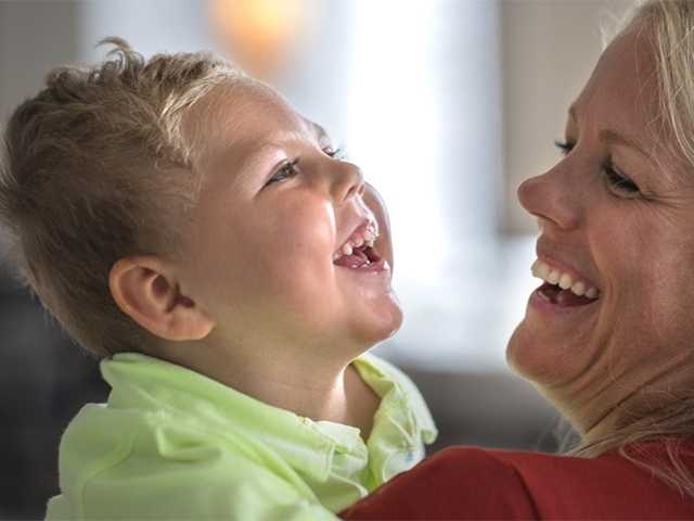 Smiling mother lifts of a smiling toddler with blonde hair