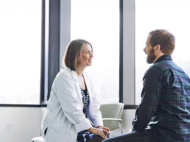 Female doctor in white lab coat sits across from male patient