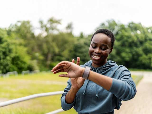 Smiling Black woman with short black hair standing outside while looking at watch on her wrist