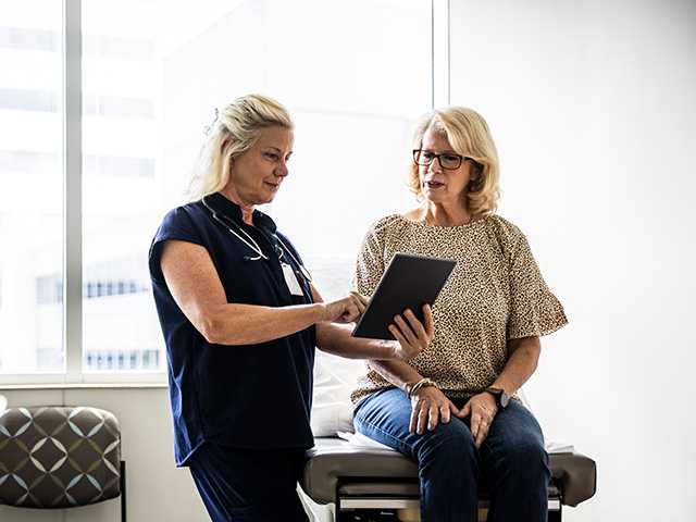 Older white woman sits on an exam table while speaking with a Corewell Health cancer care specialist