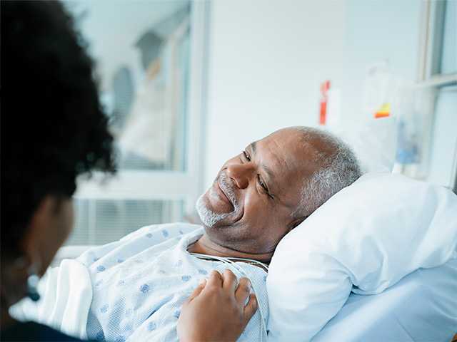 Smiling Black man laying in hospital bed looks at a woman whose hand is on his shoulder