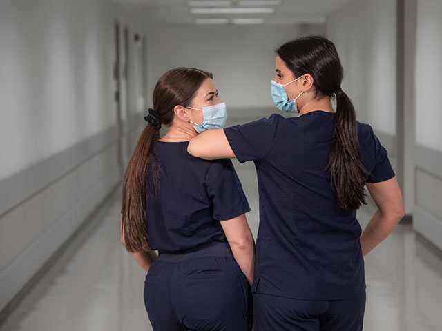 Two women wearing face masks and navy blue scrubs, standing next to each other