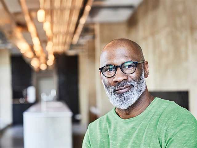 Black man with a grey beard smiles while looking at the camera