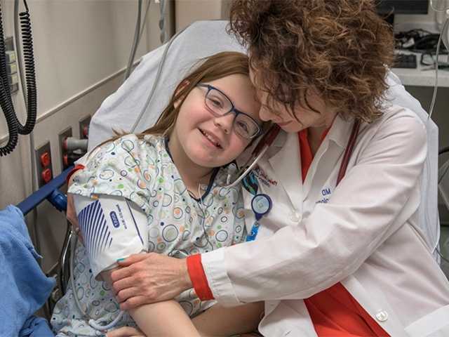 Doctor in lab coat hugs a preteen girl patient