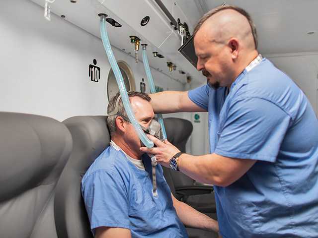 Therapist helps strap an oxygen mask on a patient sitting inside a hyperbaric oxygen chamber