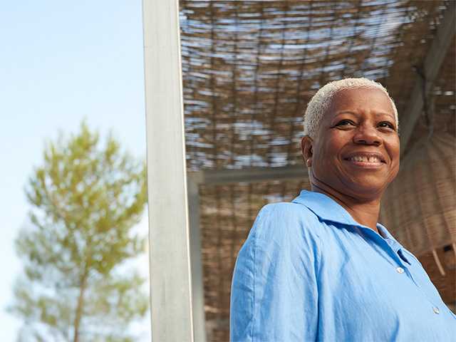 Smiling Black woman with short white hair stands in the sunshine outdoors