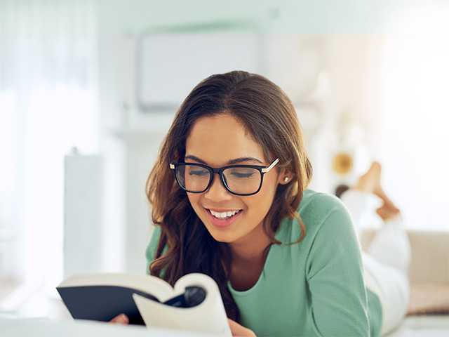 Smiling young woman with brown hair and glasses reads a book
