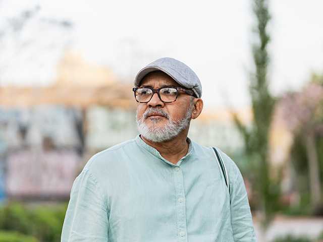 Older white man with glasses and a grey goatee stands outdoors in the evening sun