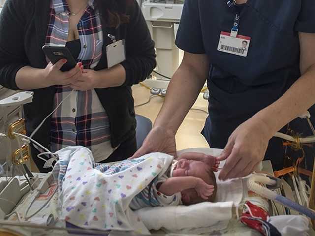 Mother and a nurse reach down to a baby inside the neonatal intensive care unit