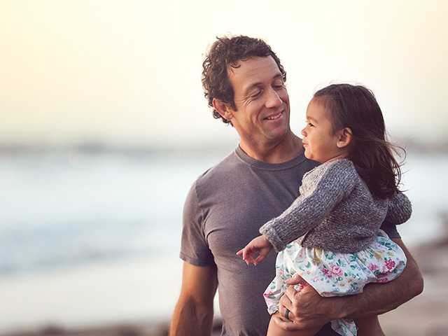 Man with curly brown hair holds his toddler daughter