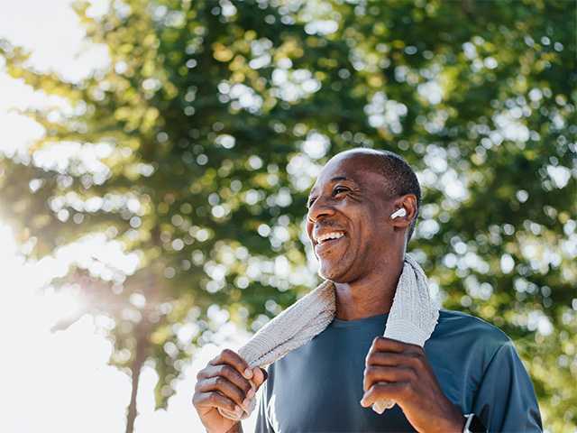 Smiling Black man stands in the sunshine with a towel around his neck after exercising