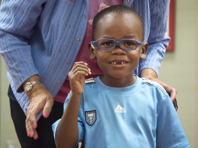 Smiling young Black boy in a light blue shirt wearing blue glasses