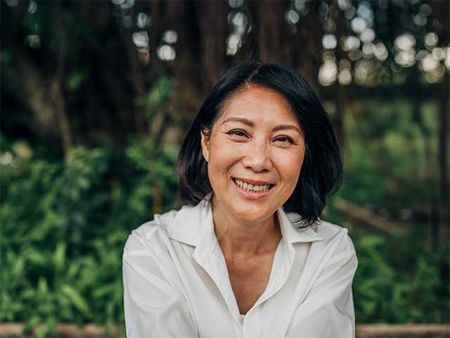 Asian woman in a white blouse sitting on a  bench in front of bushes