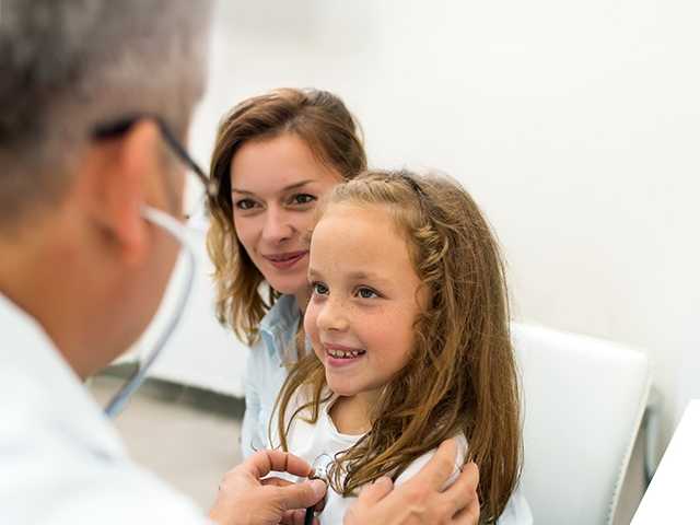 A doctor examines a young girl, who looks attentive and curious during the medical check-up.