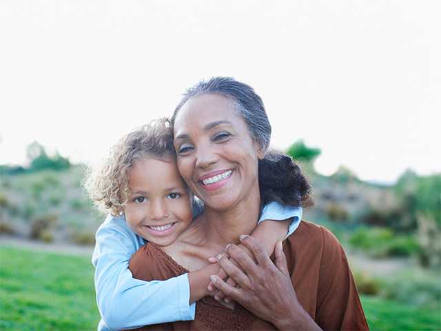 Smiling old Black woman gets a hug from her grandchild while they are outdoors