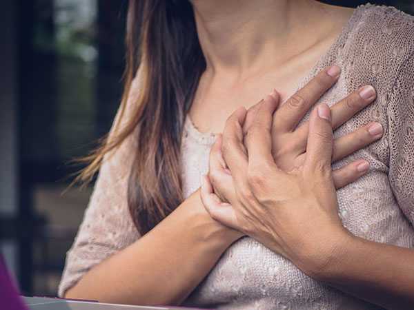Female experiencing heart attack symptoms with hands holding chest