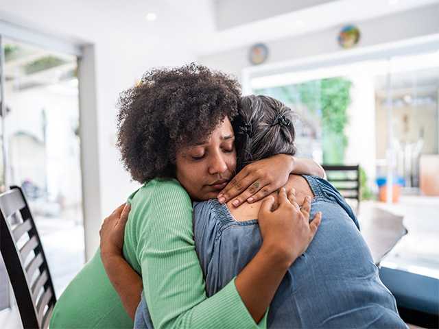 Young Black woman wearing a green shirt gets a hug from an older Black woman