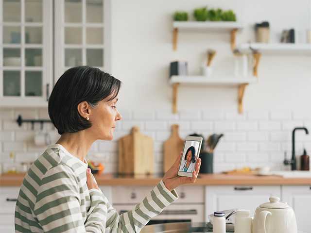 Woman in a white and green striped sweater holds up her phone while on a virtual visit with a provider