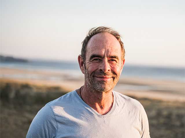 Middle aged white man stands near a beach in the sunset