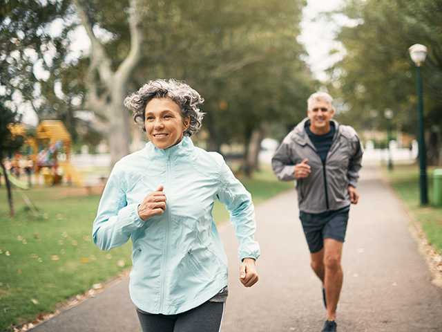 Older man and woman jog together in a park