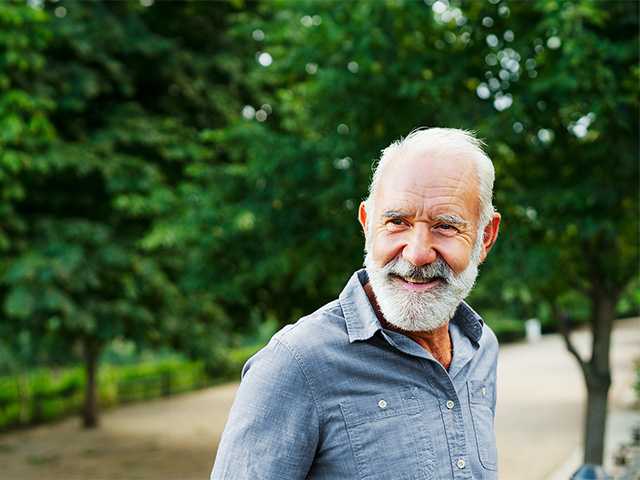 Smiling older man with white hair and white beard standing in a forest