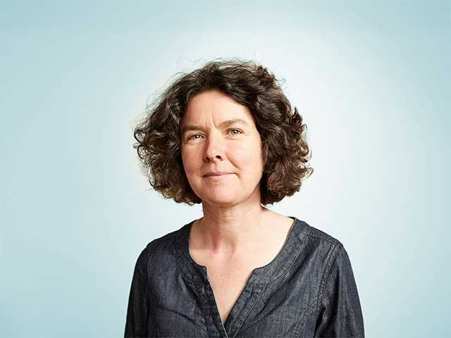 Middle aged white woman with brown hair standing in front of a light blue background