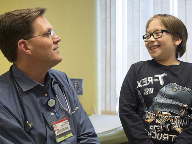 Preteen boy with glasses sits next to male doctor