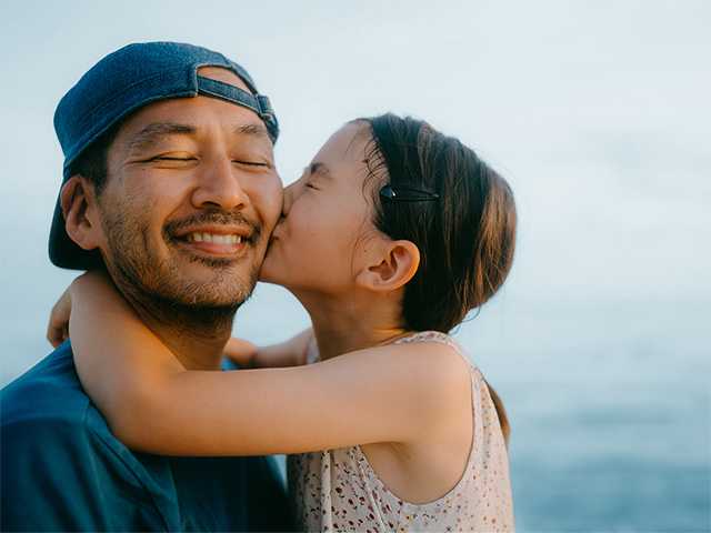 Preteen girl with long brown hair hugging her father and kissing his cheek
