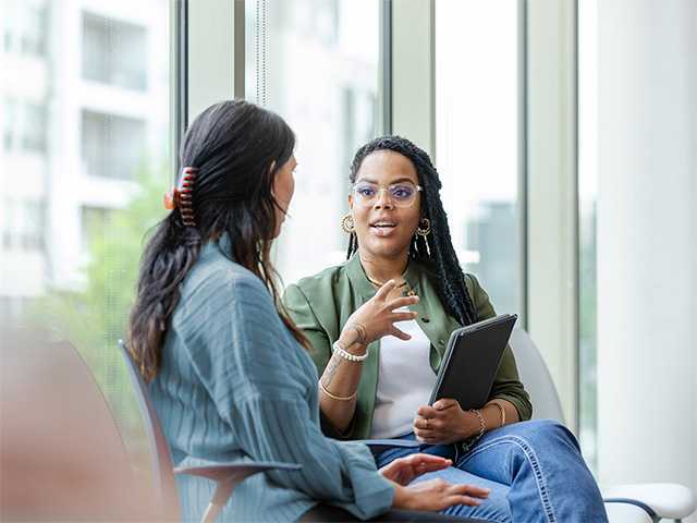 Female speech therapist sits next to a female patient while having a conversation in a speech therapy office