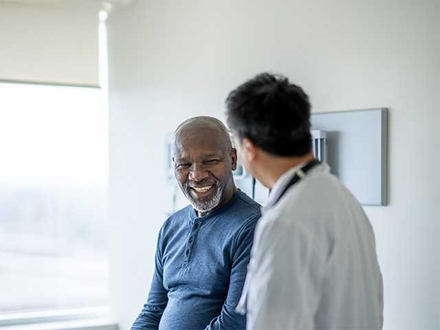 Smiling middle aged Black man speaks with a Corewell Health ear, nose, and throat surgeon in an exam room
