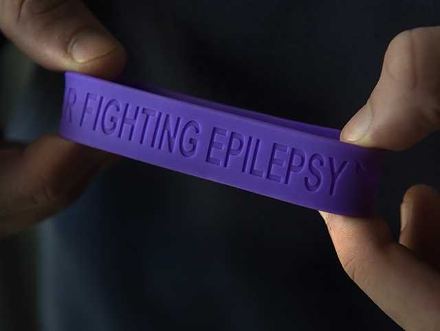 Hands holding a purple rubber bracelet with fighting epilepsy imprinted on it