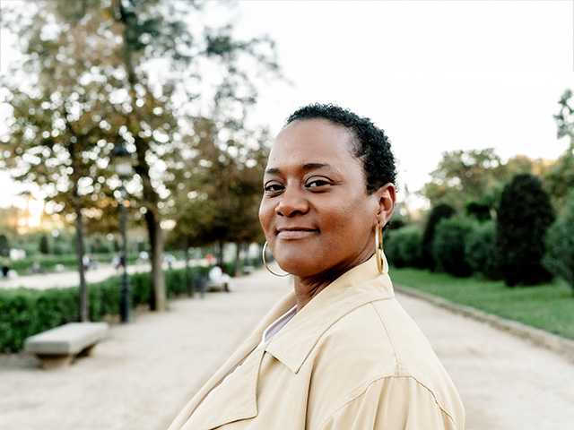 Young Black woman with short hair stands on a path in a park in the evening