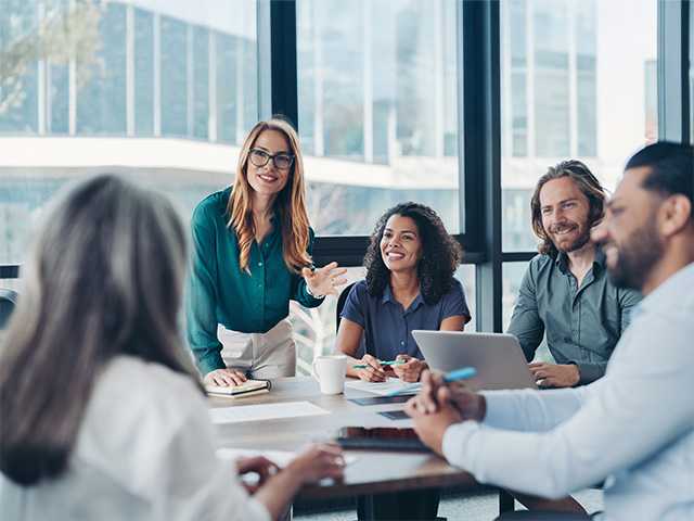 Group of business professionals sitting around a table with computers and phones having a discussion