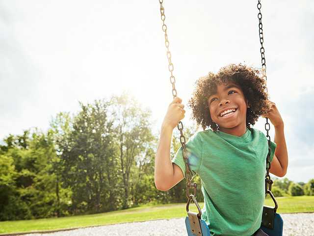 Smiling African American boy in a green t-shirt sitting on a swing