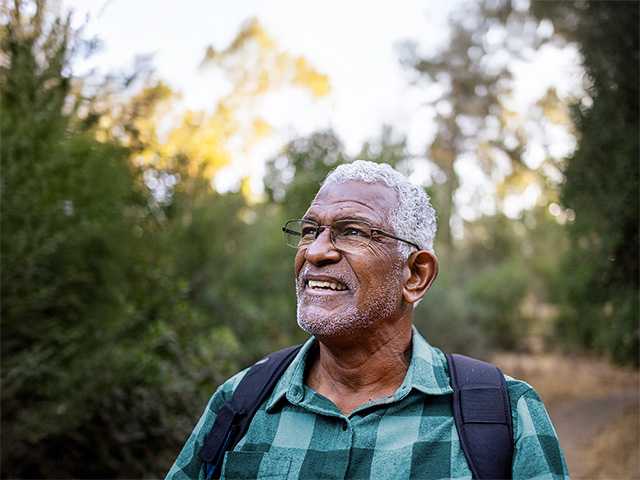 Older Black man looks at the horizon while standing outdoors in a wooded area in the evening