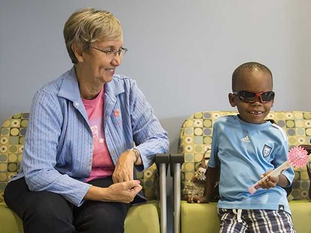 Young Black boy and his caregiver sit in chairs in waiting room