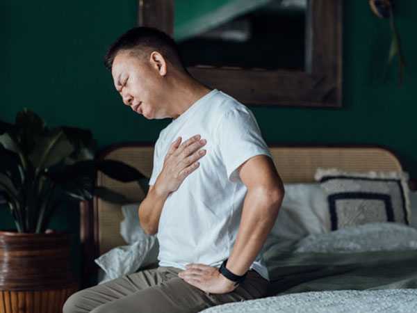 Man with heart trouble sitting in bed holding chest