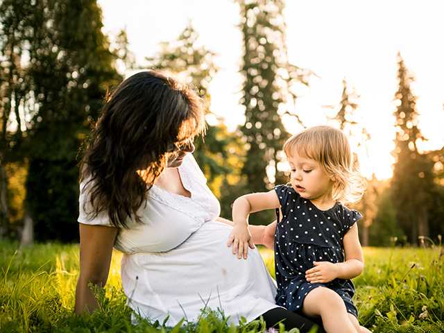 Laughing mother wearing a white dress plays with her toddler in the evening sun