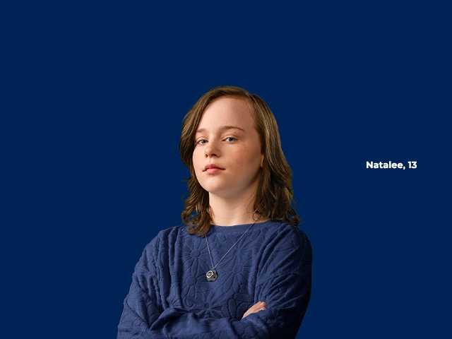 Preteen girl in a dark blue sweater standing with arms folded in front of dark blue background