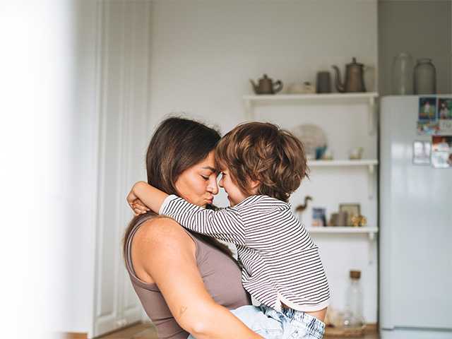 Woman lifts up and hugs a young boy as they touch foreheads